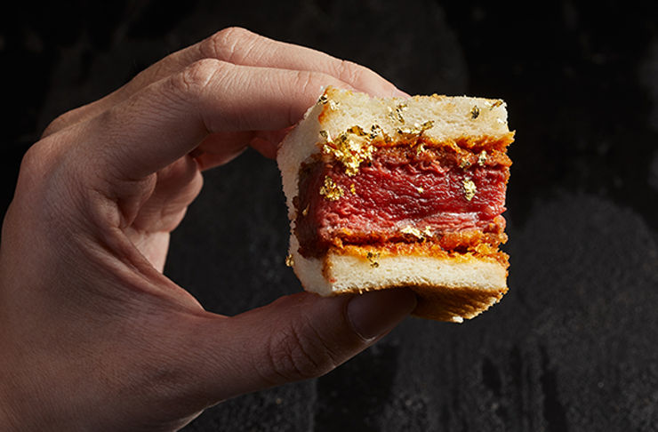 A hand holding up a sandwich filled with a rare cooked steak.